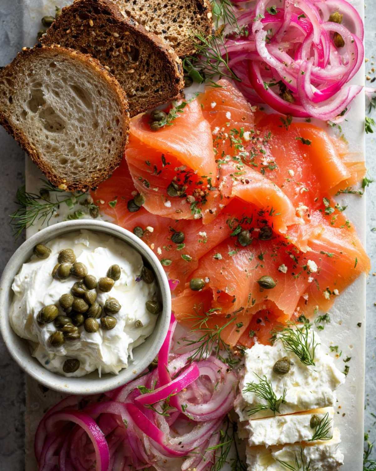 Overhead view of a Breakfast Grazing Board with Smoked Salmon, cream cheese, capers, pickled red onions, and dark bread.