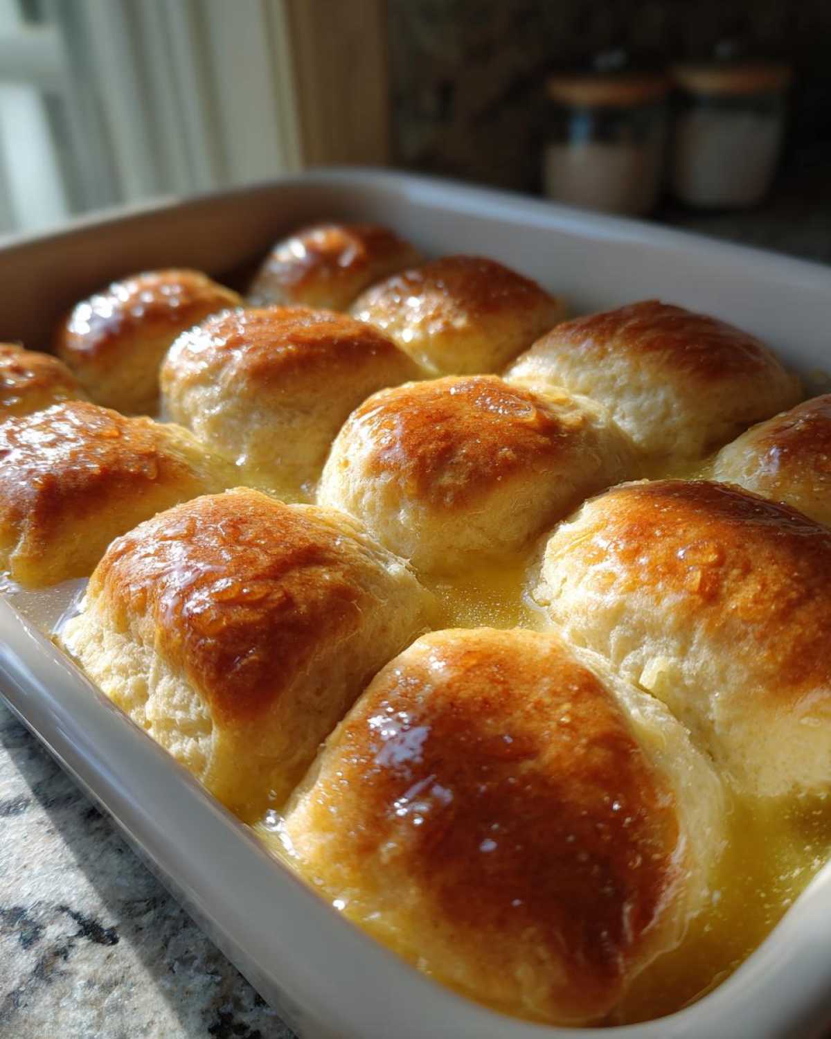 Close-up of golden brown Butter Swim Biscuits soaking in melted butter in a white baking dish.