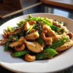 Close-up of a plate featuring Cashew Chicken Stir-Fry with bright green snap peas and glossy sauce.