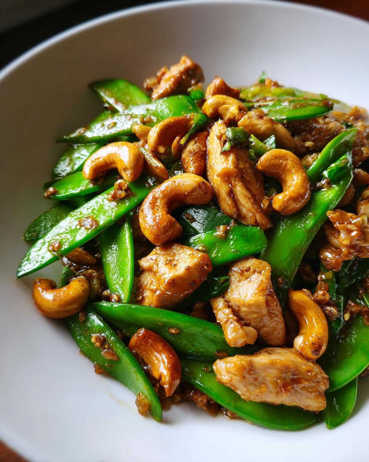 Close-up of vibrant Cashew Chicken Stir-Fry with bright green snap peas and glossy, toasted cashews.