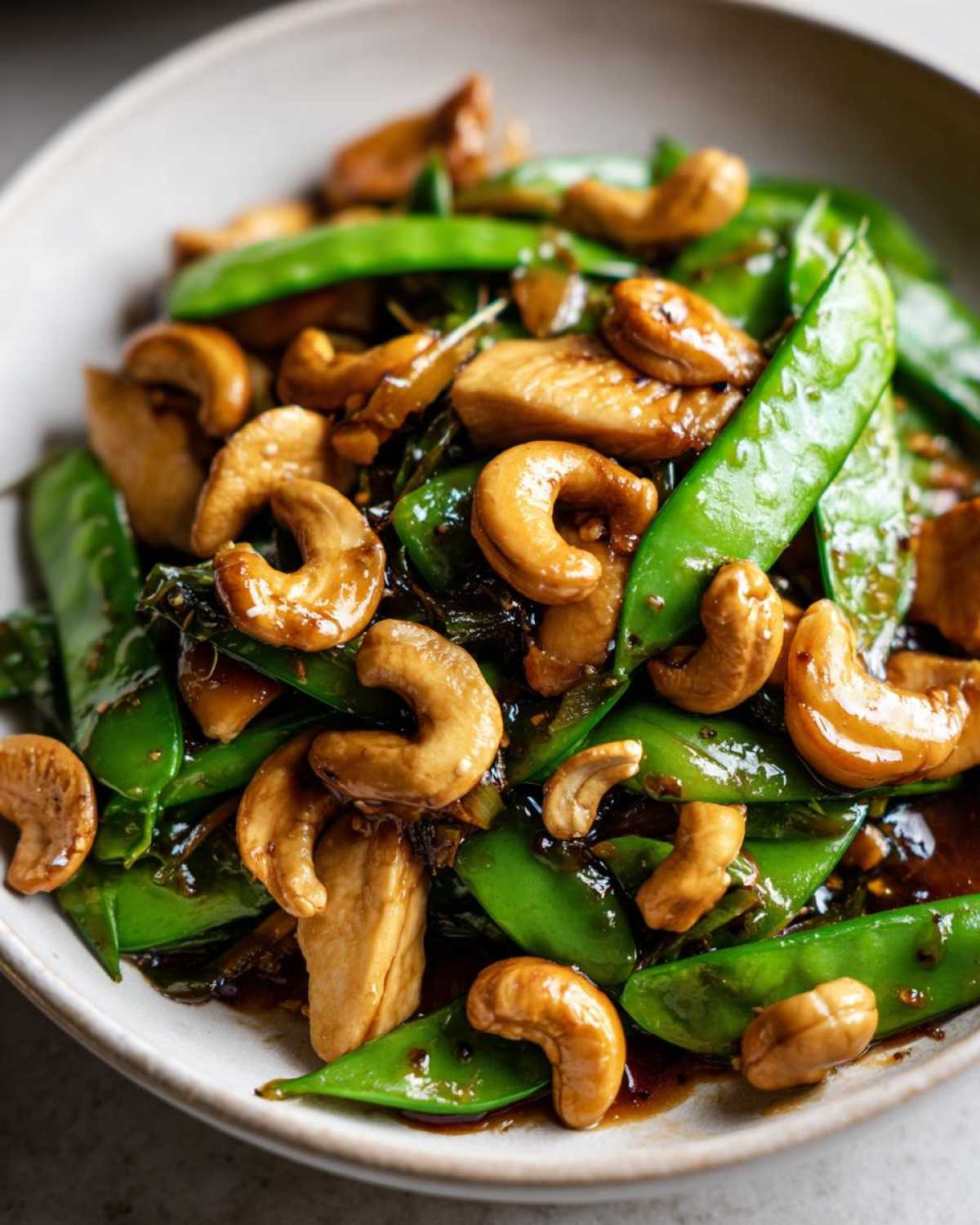 A close-up of vibrant Cashew Chicken Stir-Fry with bright green snap peas and glossy, roasted cashews in a savory sauce.