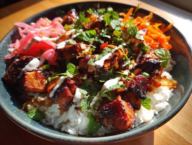 Close-up of a vibrant Chicken Banh Mi Bowl featuring glazed chicken pieces over rice, topped with pickled vegetables and fresh mint.