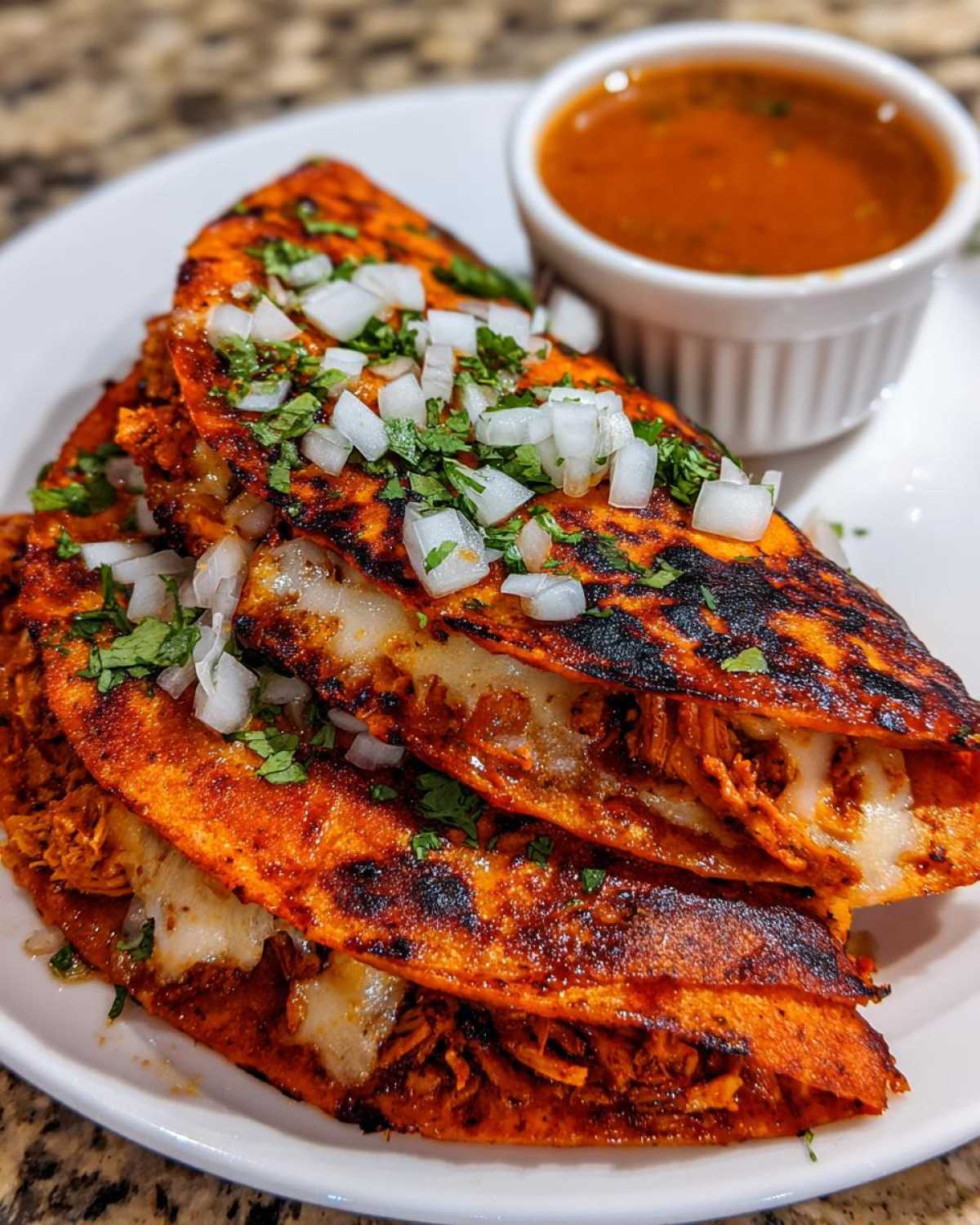 Three crispy, red-stained Chicken Birria Tacos topped with diced white onion and cilantro, served with a side of consomé.