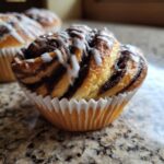 A close-up of a freshly baked Chocolate Hazelnut Babka Bun swirled with chocolate filling and drizzled with white icing.