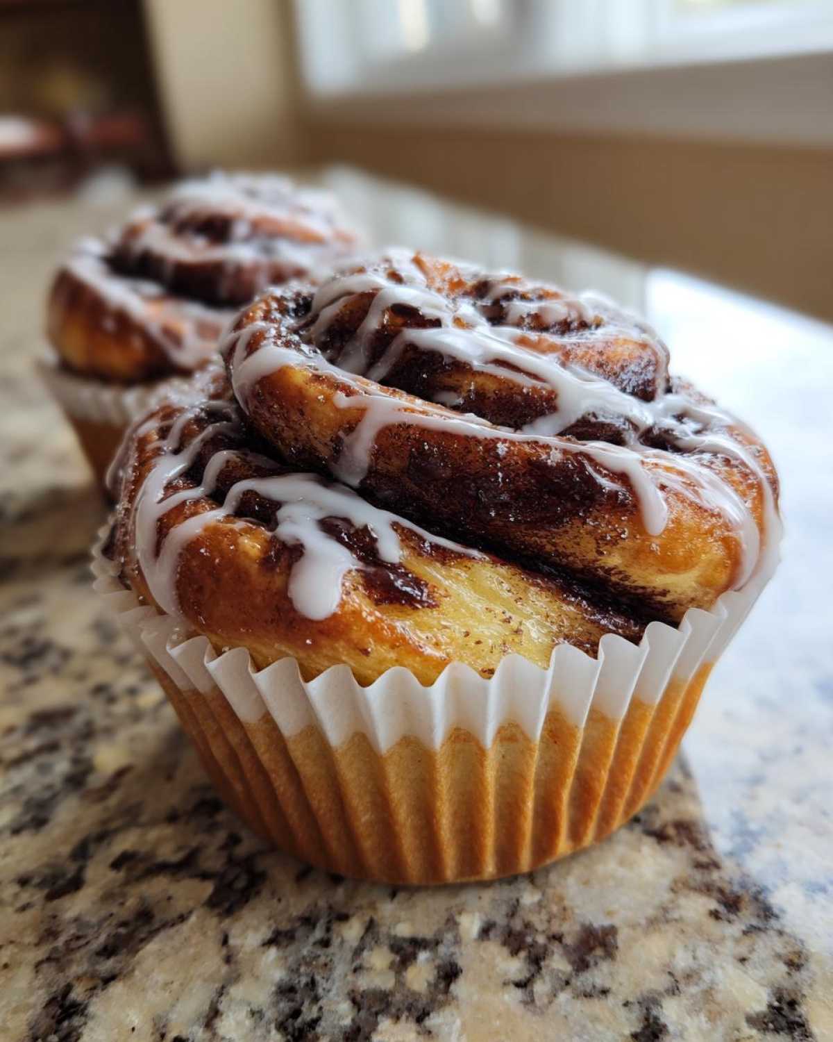 Close-up of a freshly baked Chocolate Hazelnut Babka Bun topped with white icing, sitting in a paper liner.