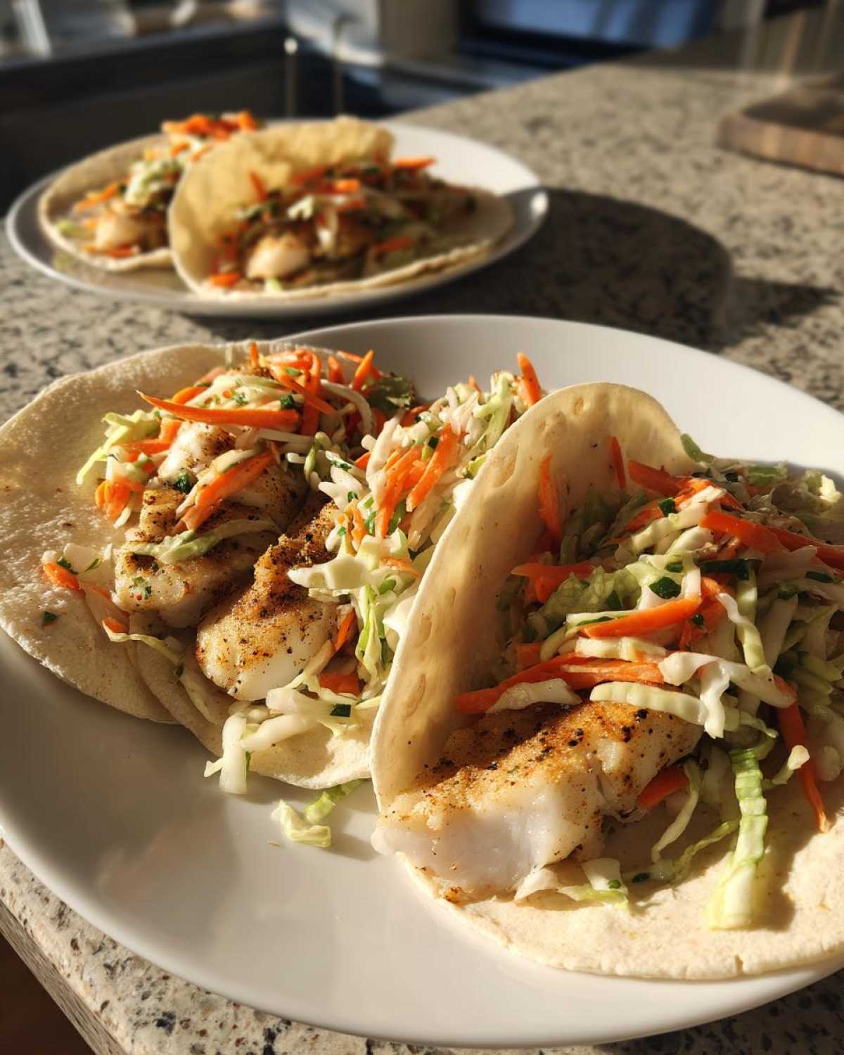 Two Cod Fish Tacos filled with seasoned white fish and vibrant crunchy slaw on a white plate.