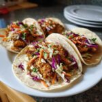 Four delicious Cod Fish Tacos topped with vibrant, crunchy slaw featuring red cabbage and carrots.