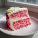 A tempting slice of Cortadillo Mexican Pink Cake featuring bright pink layers and white frosting, served on a white plate.