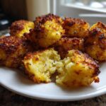 A pile of golden brown Crispy Garlic Parmesan Crusted Potatoes bites on a white plate, one is broken open.