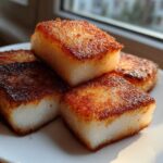 Four golden-brown, pan-fried squares of Crispy Shanghai Butter Mochi stacked on a white plate.