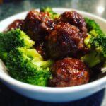 Close-up of glossy Crockpot Teriyaki Meatballs with bright green steamed broccoli florets in a white bowl.