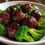 Close-up of glossy Crockpot Teriyaki Meatballs with Broccoli florets in a white bowl.