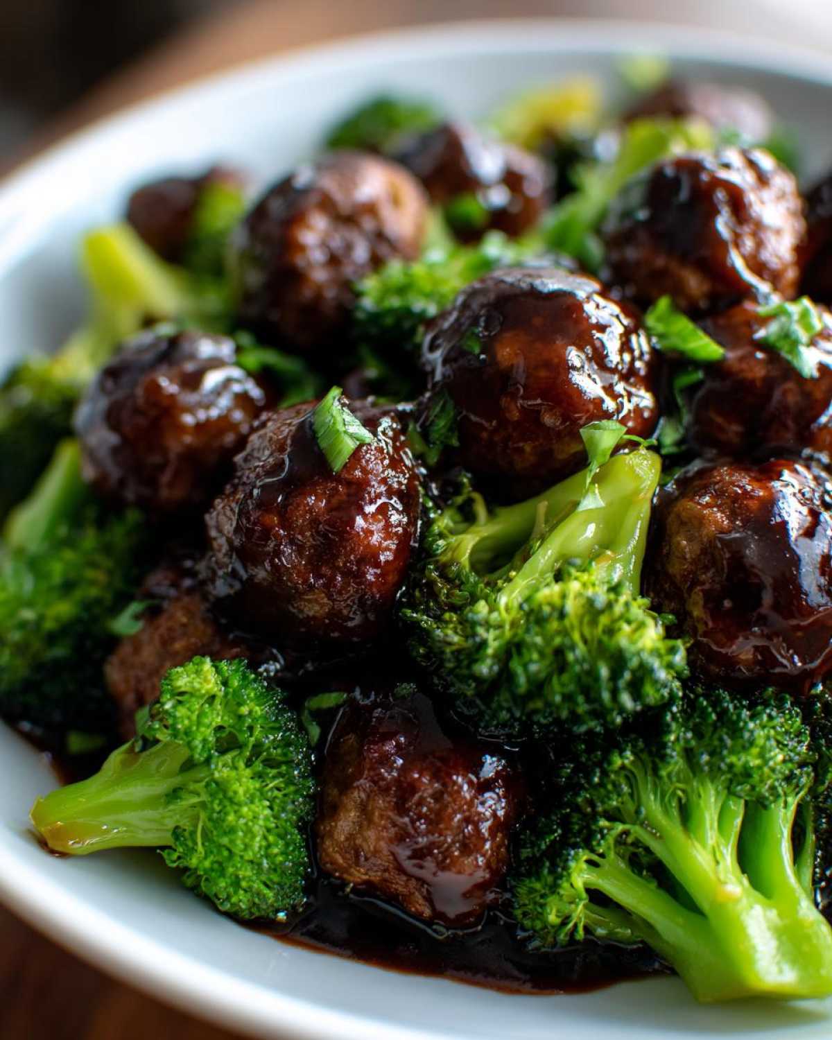 A close-up of glossy Crockpot Teriyaki Meatballs coated in dark sauce, served over bright green steamed broccoli florets.