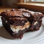 A rich, fudgy square of Deviled Brownies with Marshmallow Filling showing a gooey white center.