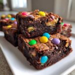 Close-up of fudgy Easter Egg Brownies with Peanut Butter stacked on a white plate, topped with colorful candy eggs.