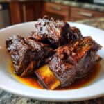 Close-up of tender, dark, braised Filipino Beef Short Ribs Adobo pieces in a white bowl with rich sauce.