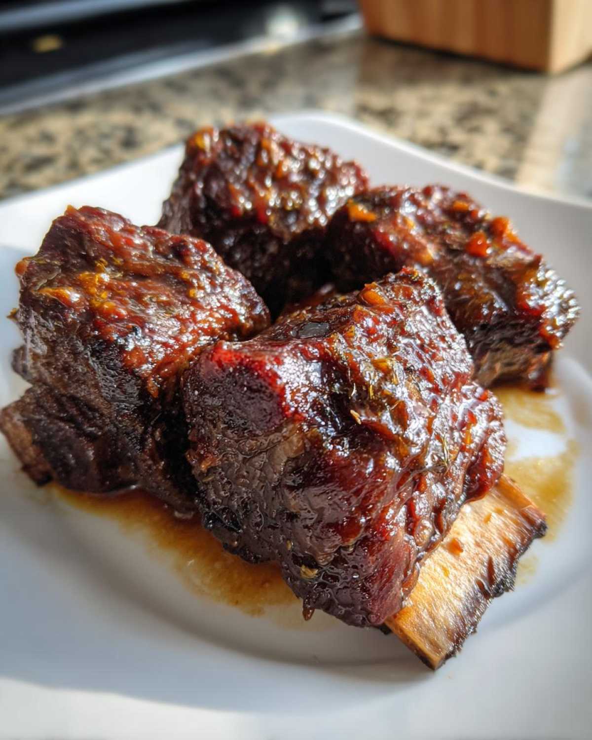 Four tender, glazed pieces of Filipino Beef Short Ribs Adobo served on a white plate.
