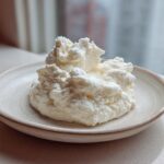 A mound of white, fluffy 2-Ingredient Fluffy Cloud Dough sitting on a small, speckled ceramic plate.