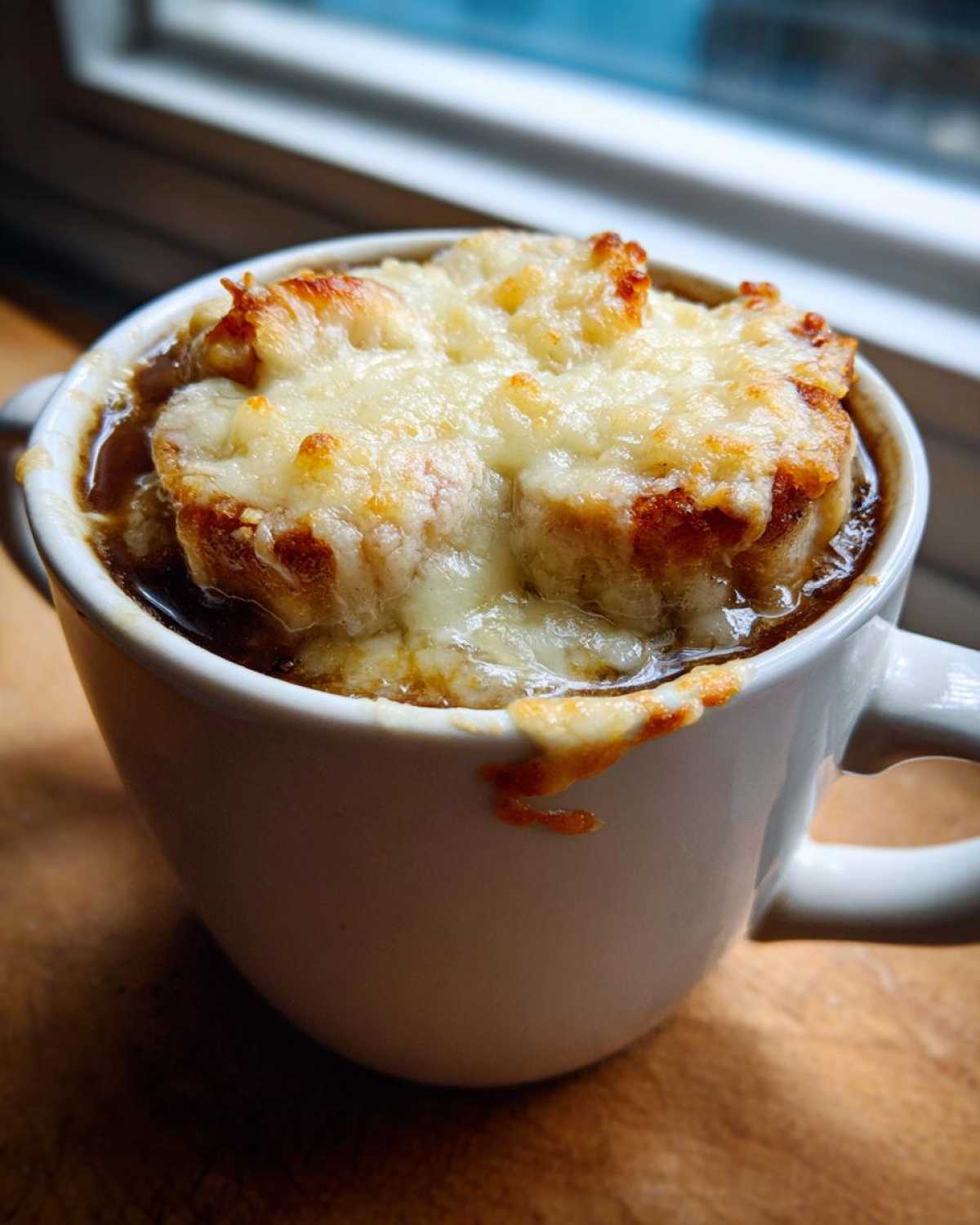 Close-up of French Onion Gnocchi Soup topped with melted, browned cheese over croutons in a white mug.