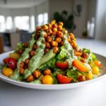 A vibrant Green Goddess Salad topped with a mound of crispy chickpeas and creamy green dressing.