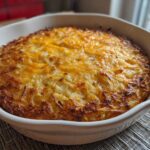 A close-up of golden brown Hash Browns in Oven with Cheesy Crust baked in a white oval casserole dish.