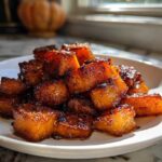 Close-up of caramelized Hot Honey Melting Sweet Potatoes cubes piled high on a white plate.