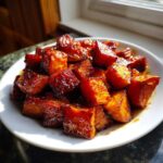 Close-up of cubed Hot Honey Melting Sweet Potatoes, glistening with a rich, dark glaze, served on a white plate.