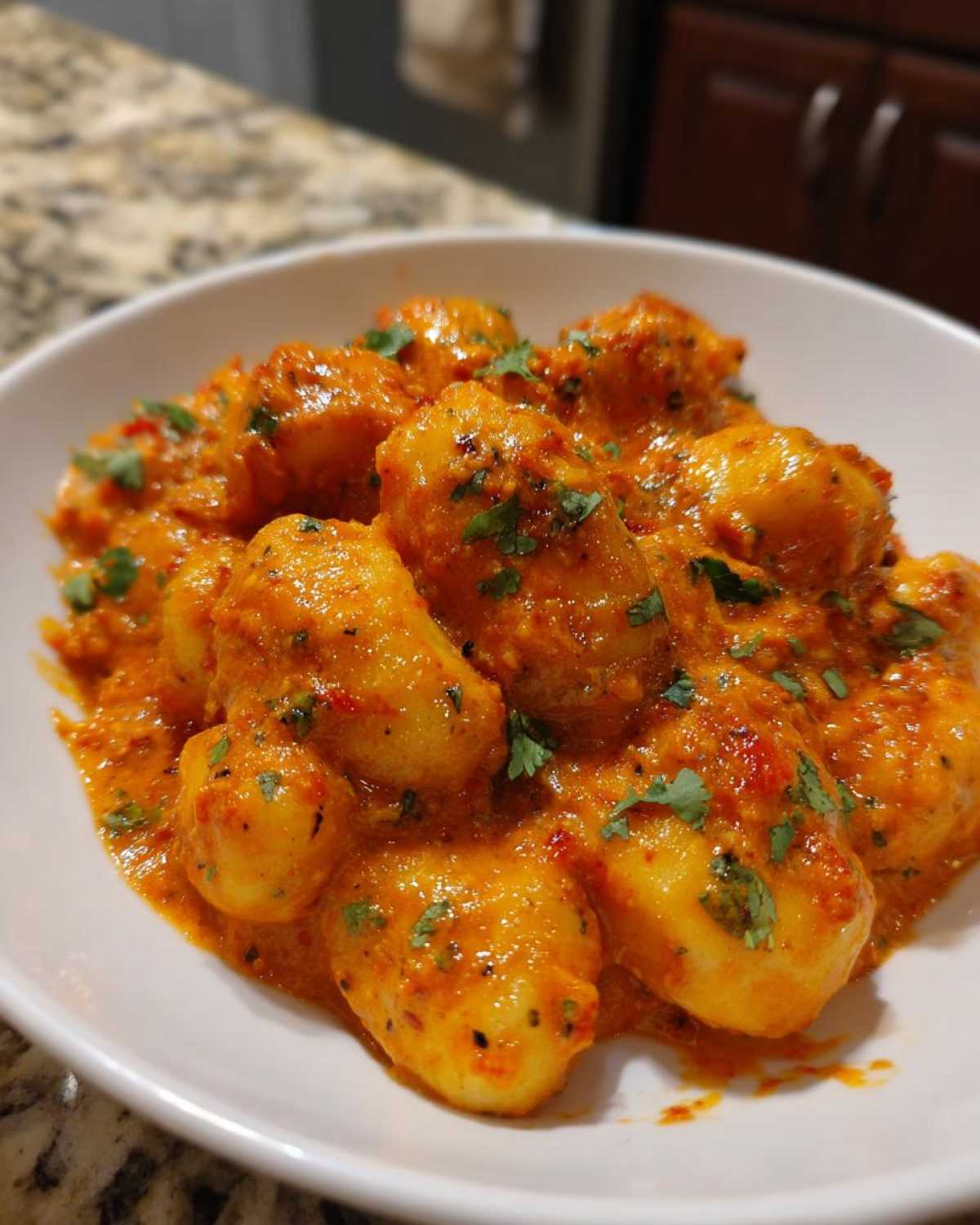 A white bowl filled with tender gnocchi coated in a rich, creamy, orange-red sauce, garnished with fresh cilantro, representing Indian-Style Butter Gnocchi.
