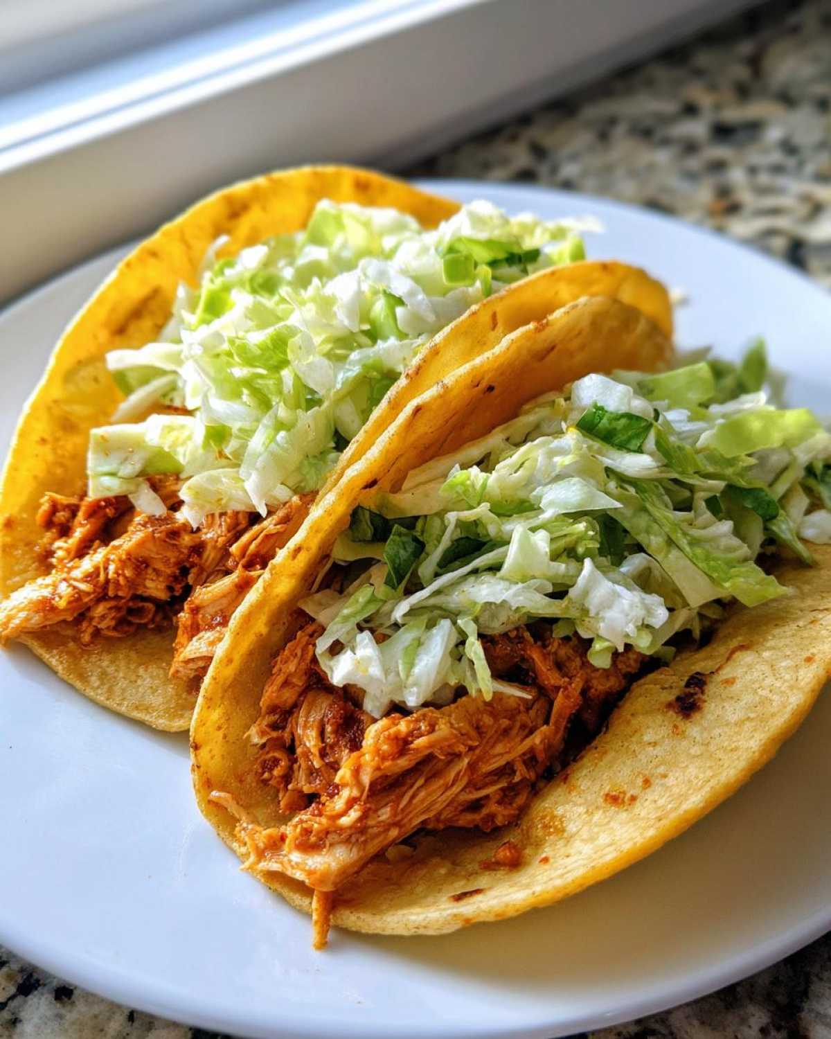 Close-up of two soft corn tortillas filled with shredded chicken and topped generously with shredded cabbage for Instant Pot Chicken Tacos.