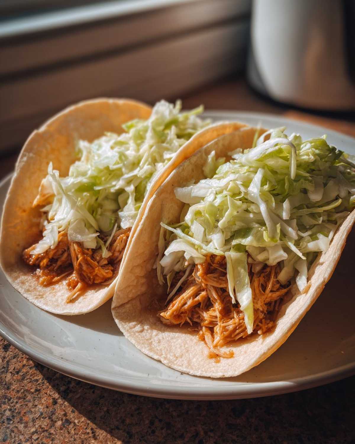 Two soft shell tacos filled with shredded chicken and topped generously with shredded cabbage, ready to eat.