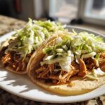 Two soft corn tortillas filled with shredded chicken and topped with fresh shredded cabbage for Instant Pot Chicken Tacos.