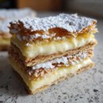 Two stacked squares of delicious Karpatka Cake (Polish Cream Cake) featuring flaky pastry and thick vanilla cream, dusted with powdered sugar.