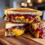 Cross-section of a grilled Leftover Meatloaf Sandwich with spicy glaze, melted cheddar cheese, and jam on toasted bread.