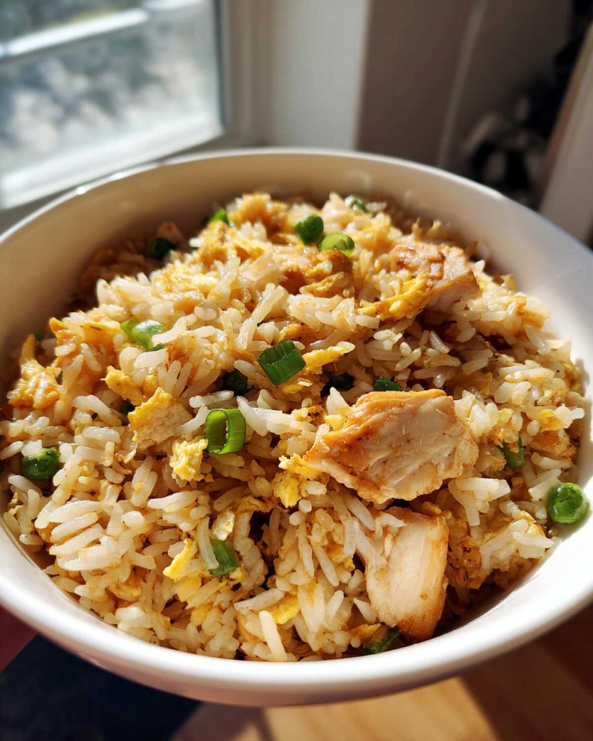 Close-up of a white bowl filled with Leftover Rotisserie Chicken Fried Rice, featuring rice, scrambled egg, and green onions.