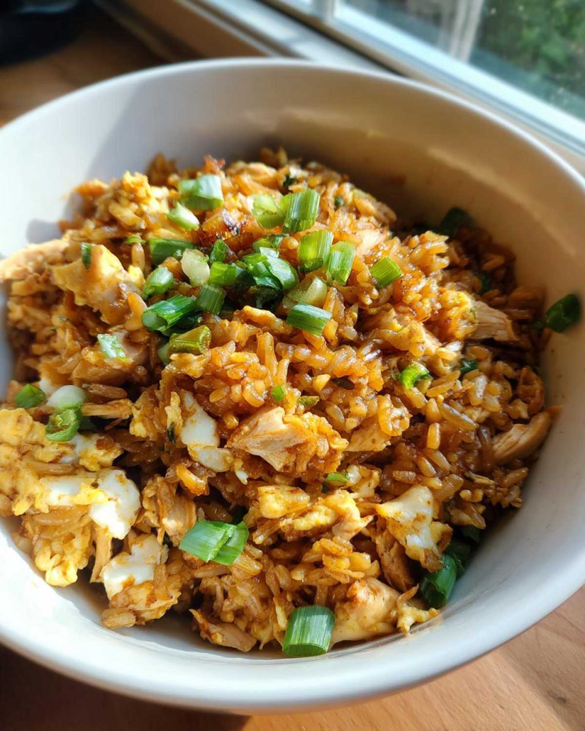 A close-up of a white bowl filled with savory Leftover Rotisserie Chicken Fried Rice, topped with fresh green onions.