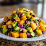 A close-up, appetizing mound of fresh Mango Avocado Salsa with Black Beans, featuring diced mango, avocado, red onion, and black beans.