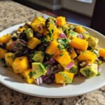 A close-up of a white plate filled with colorful Mango Avocado Salsa with Black Beans, featuring diced mango, avocado, red onion, and cilantro.
