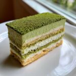 A perfect slice of 8-Layer Matcha Tiramisu with Ladyfingers showing alternating layers of green cream, white cream, and soaked ladyfingers.