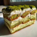 A close-up slice of layered Matcha Tiramisu with Ladyfingers, topped with green matcha powder.