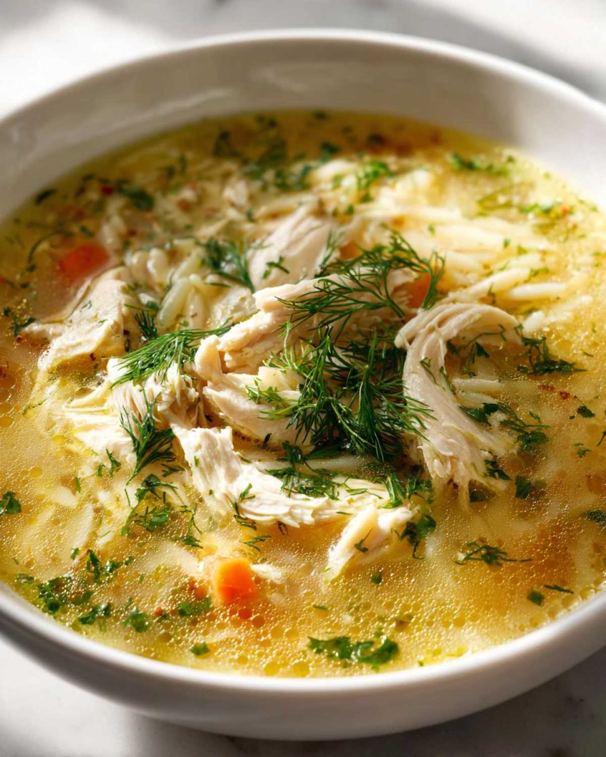 Close-up of a bowl of Mediterranean Lemon Chicken Soup with Orzo, featuring shredded chicken and fresh dill.