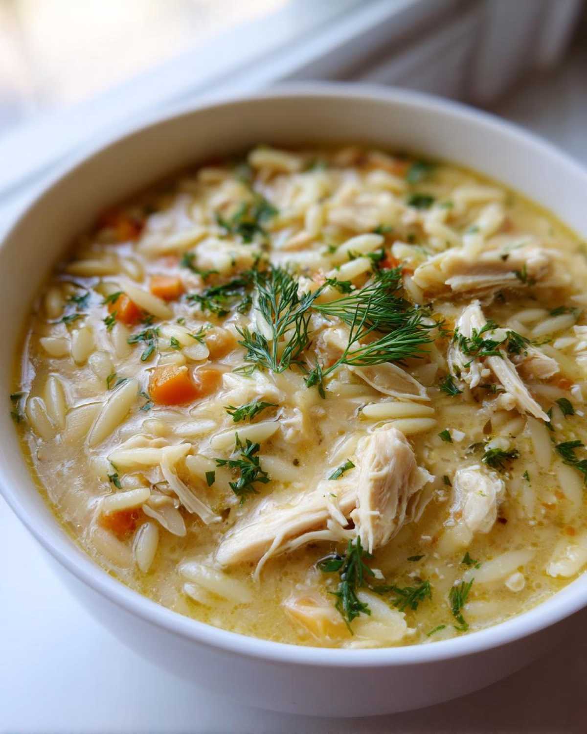 Close-up of a hearty bowl of Mediterranean Lemon Chicken Soup with Orzo, garnished with fresh dill.