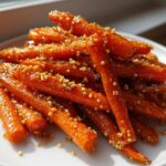 A pile of glazed Miso Maple Carrots with Crunchy Quinoa sprinkled over them, served on a white plate.