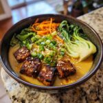 A close-up of delicious Miso Peanut Ramen Bowls with Tofu, topped with scallions, shredded carrots, and bok choy.