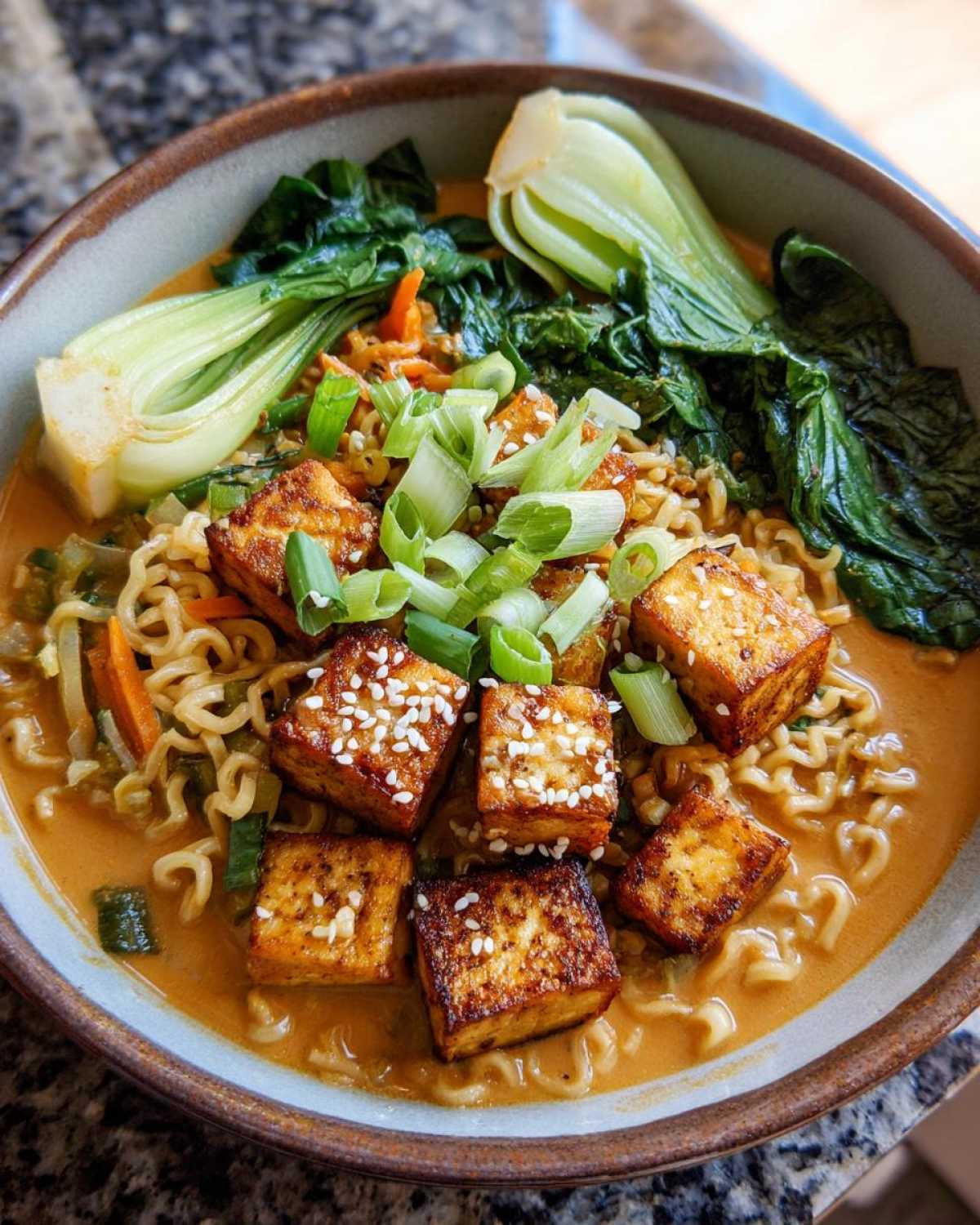 A close-up view of a bowl of Miso Peanut Ramen Bowls with Tofu, featuring crispy tofu cubes and bok choy.