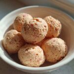 A white bowl filled with several No-Bake Strawberry Shortcake Protein Bites, showing flecks of red strawberry throughout.