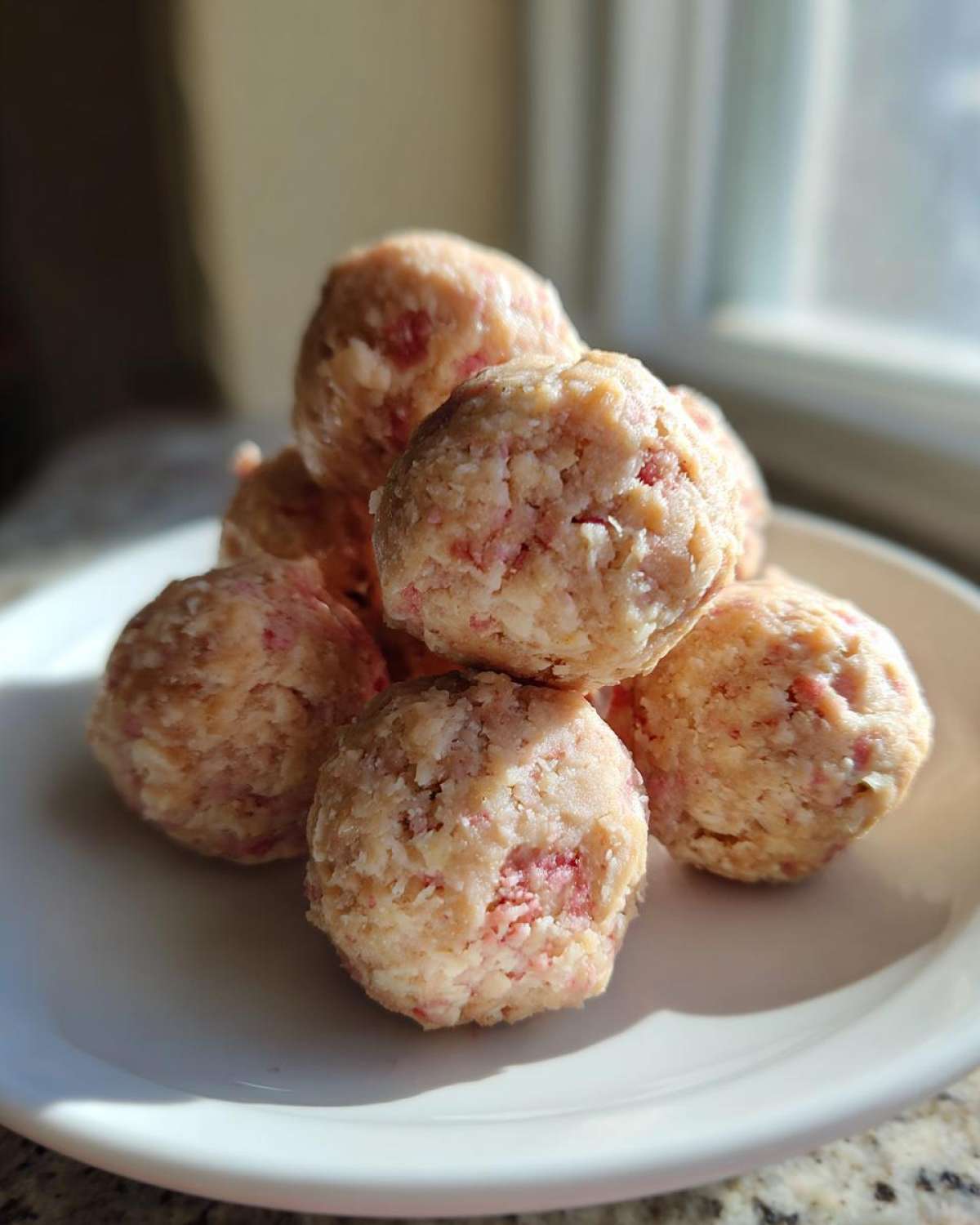 A small stack of No-Bake Strawberry Shortcake Protein Bites on a white plate, showing pink strawberry flecks.