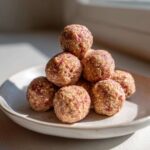 A stack of No-Bake Strawberry Shortcake Protein Bites piled on a light-colored speckled plate, illuminated by natural light.