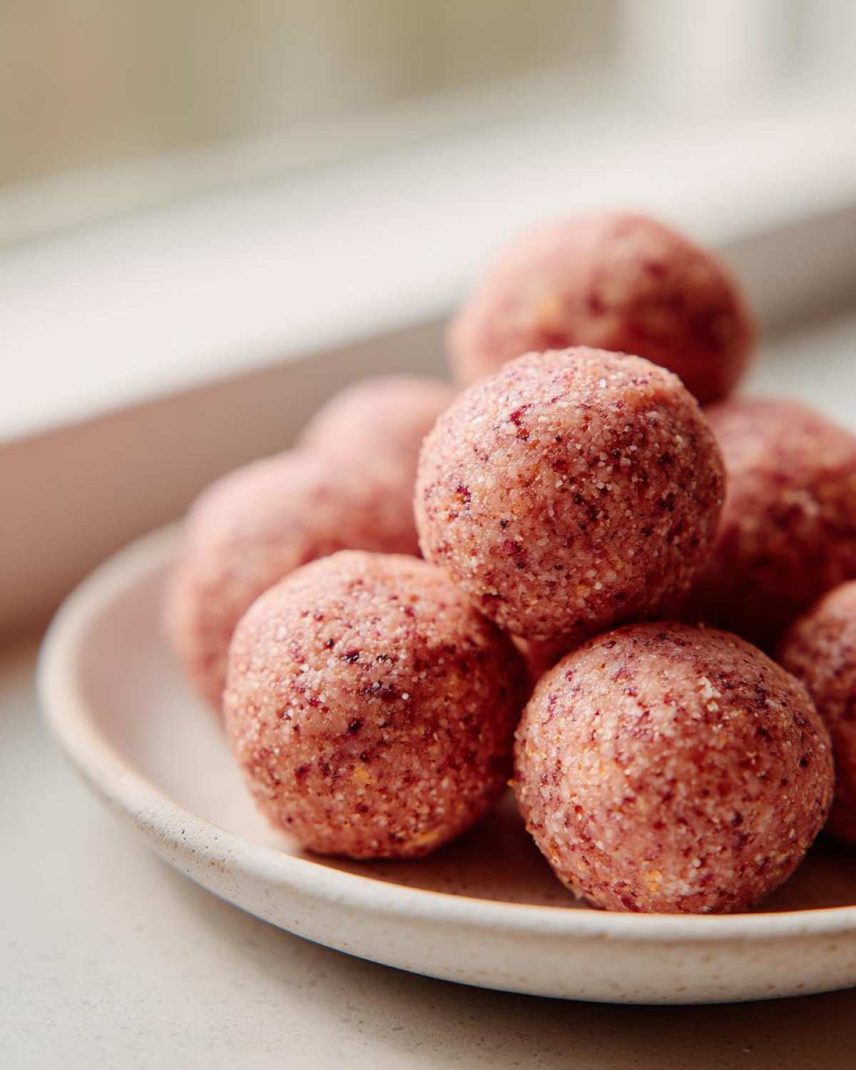 A stack of pink, textured No-Bake Strawberry Shortcake Protein Bites resting on a small, light-colored ceramic plate.