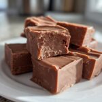 A stack of rich, square pieces of No-Fail Fudge with Milk Chocolate on a white plate.