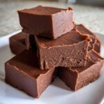 A stack of rich, dark brown squares of No-Fail Fudge with Milk Chocolate piled on a white plate.